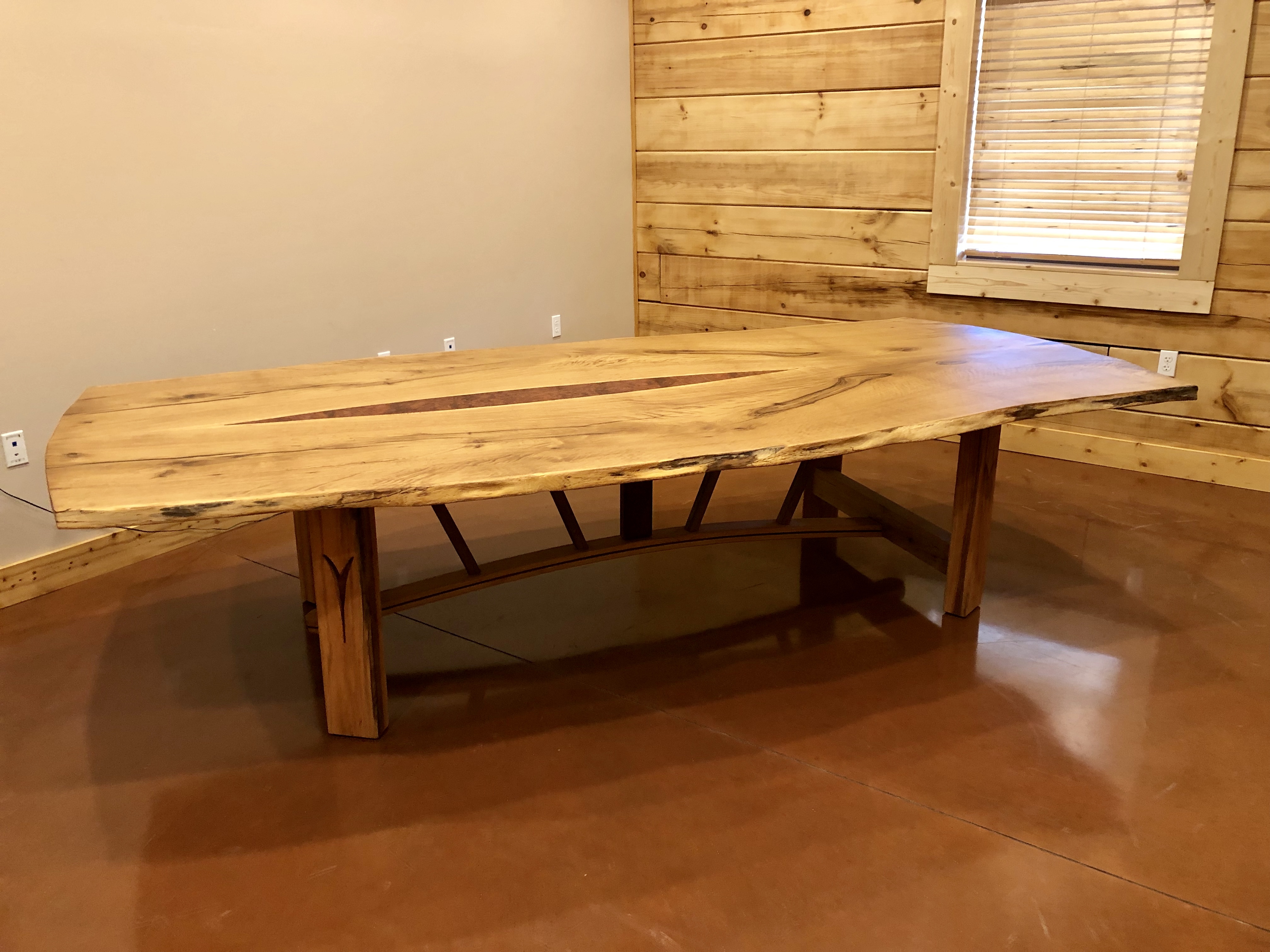 Large live edge conference table made of red oak. the dementions of this table are six feet wide and ten feet long. this table features a trestle style base with custom inlay built into the legs.
